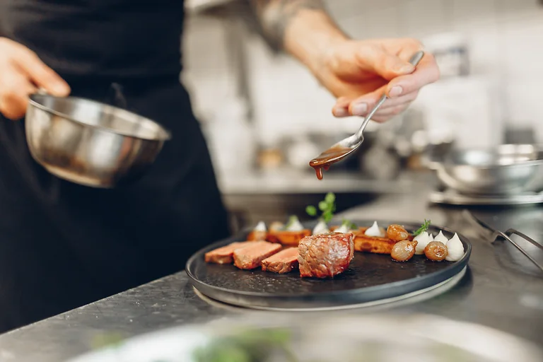 Ein Koch verfeinert kunstvoll angerichtetes Rinderfilet mit Sauce im Genuss-Atelier Dresden.