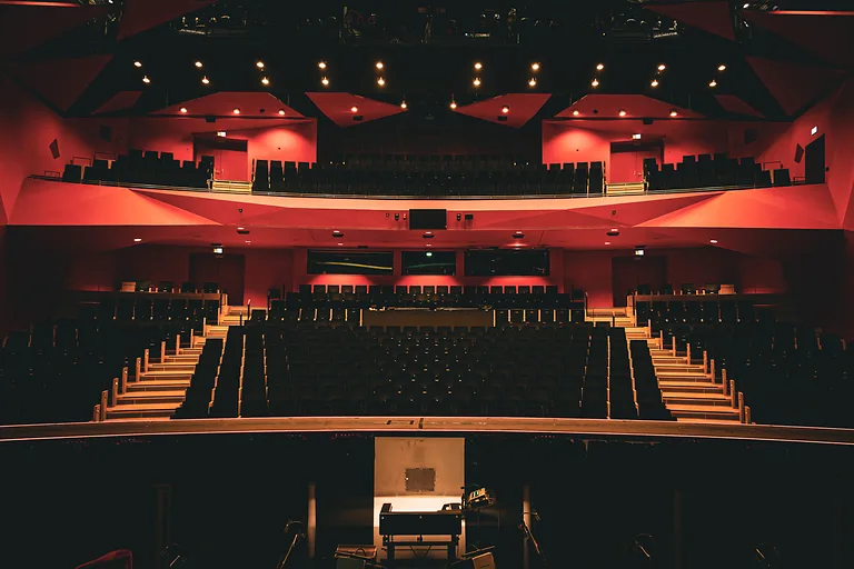 View from the stage into the red illuminated auditorium of Dresden State Operetta with symmetrical architecture.