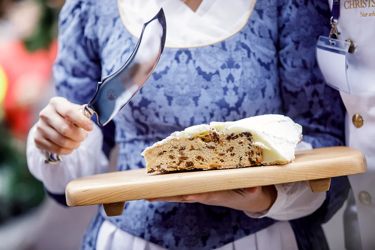 Nahaufnahme: Stollenmädchen hält einen angeschnittenen Riesenstollen und ein Stollenmesser auf dem Striezelmarkt