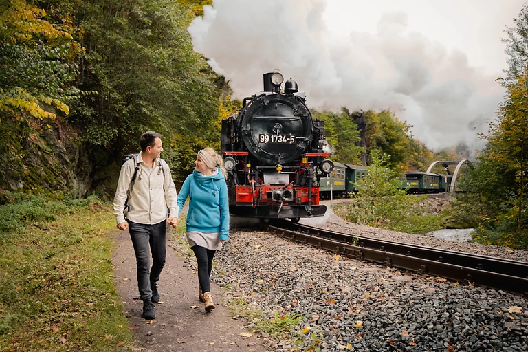 Couple hiking along the Weißeritztalbahn in the Dresden Elbland as the steam train approaches from behind.