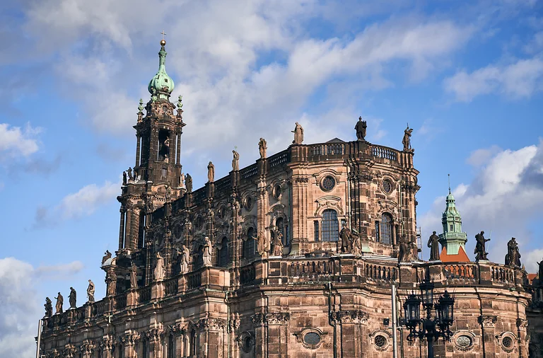 Blick auf einen Turm der Hofkirche Dresden mit angrenzendem Gebäudeteil und Himmel im Hintergrund.