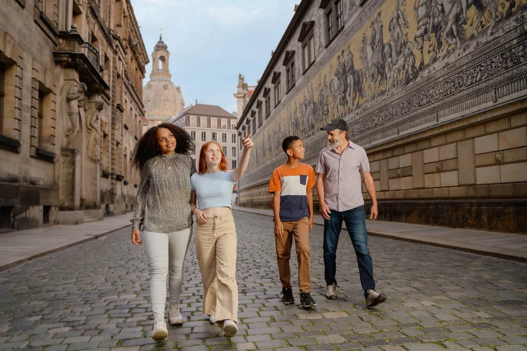 Familie spaziert am Fürstenzug vorbei, im Hintergrund ist die Dresdner Frauenkirche zu sehen.