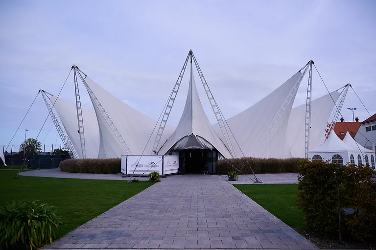 Außenansicht des weißen Zirkuszelts Ostra Dome in Dresden mit freier Fläche davor.
