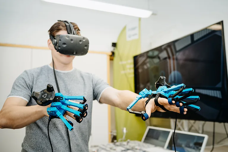 Eine Person testet eine VR-Brille und spezielle Roboter-Handschuhe.