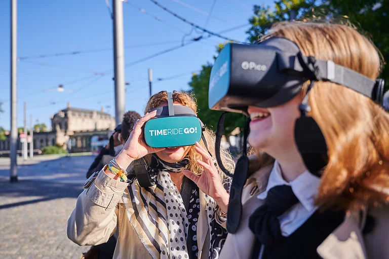 Teilnehmende der VR-Route mit TimeRideGo! in der Dresdner Altstadt. Vorn rechts eine Frau im Profil, zentral eine Frau mit VR-Brille.