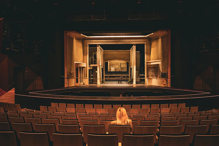 Visitor sits in the auditorium of Dresden State Operetta looking toward the illuminated stage.