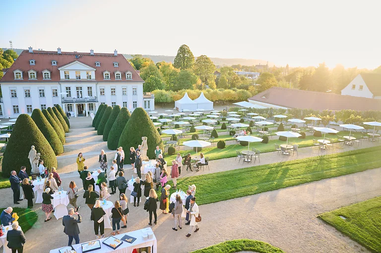 Schloss Wackerbarth bei Sonnenschein mit Sektempfang und Häppchen im Außenbereich, Gäste genießen die Atmosphäre.