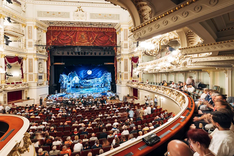 Blick in den vollbesetzten Zuschauerraum der Semperoper Dresden mit beleuchteter Bühne.